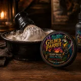 A tin of Gilded Parrot Beard Balm beside its box, on a dark ground