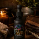 A bottle of Gilded Parrot Beard Oil beside its box, on a dark ground