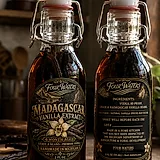 Three bottles of Four Waters Vanilla Extract on a board with a bundle of vanilla beans